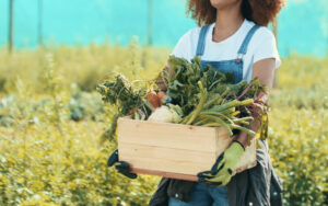 woman outside holding a basket overflowing with garden harvest